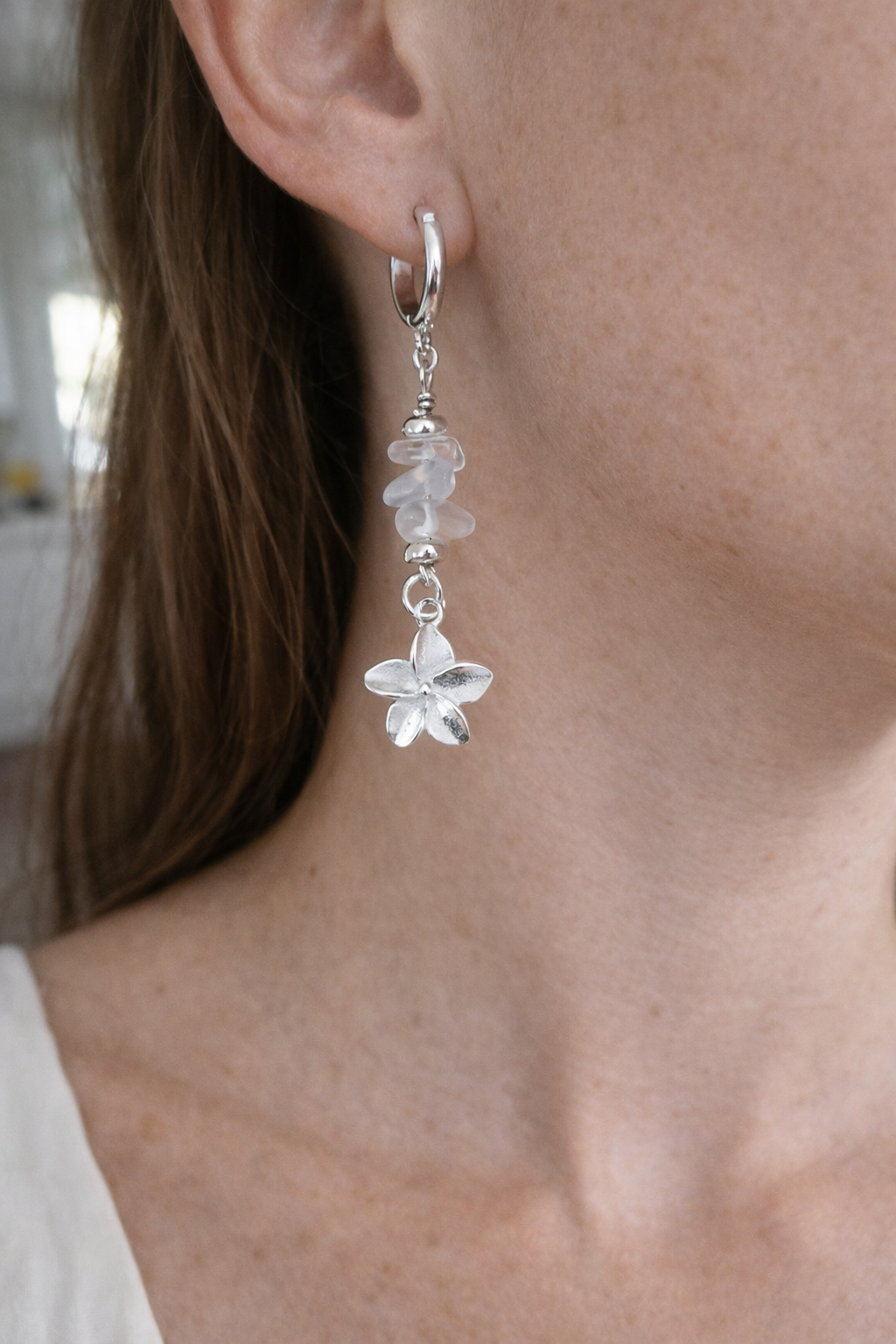 Silver plumeria drop earrings resting on olive wood